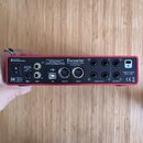 Červený rackový audio rozhraní s nápisem Focusrite a webovou adresou www.focusrite.com. Na předním panelu jsou umístěny konektory USB, MIDI OUT, MIDI…