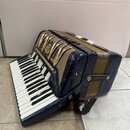 Modře mramorovaná akordeon s klávesnicí a zlatými kovovými prvky. Na předním krytu je vidět oválný štítek s nápisem "Scherzino". Nástroj vykazuje zná…