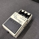 Bílý efekt pedál Boss Noise Suppressor NS-2 v kompaktním kovovém provedení s černým gumovým spínacím pedálem. Na horní části jsou čtyři bílé ovládací…