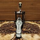 Černý bicí pedál s kovovými a stříbrnými prvky. Na šlapce je vidět logo MAPEX v oválném rámečku. Povrch pedálu vykazuje mírné známky používání a drob…