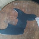 Černý plastový pickguard pro elektrickou kytaru s několika otvory pro šrouby. Vedle něj je průhledný plastový sáček s několika malými šroubky. Předmě…