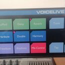Detailní pohled na ovládací panel zařízení s nápisem VOICELIVE RACK. Panel obsahuje mřížku barevných tlačítek s popisky: μMod, Delay, Reverb, Tone, P…