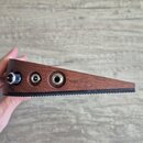 Detailní pohled na hranu hnědého dřevěného zařízení s kovovými prvky. Na povrchu jsou umístěny dva konektory a jeden regulační knoflík, u kterých je…