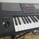 Černý digitální klavír s nápisem KORG na předním panelu. V pravém horním rohu je označení Pa700 PROFESSIONAL ARRANGER a displej. Nástroj má bílé a če…