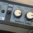 Detailní záběr na ovládací panel kytarového komba v šedé barvě. Jsou vidět ovratidla s bílými vršeky a nápisy VOLUME, CHORUS, AUX, CENTER CANCEL, TON…
