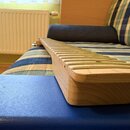 Dřevěný nástroj s řadou paralelních kovových strun natažených přes dřevěné mostky. Nástroj má světle hnědou barvu a hranatý tvar rezonátoru. Na povrc…
