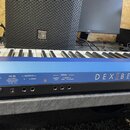 Detailní pohled na zadní panel modrého digitálního piana s nápisem DEXIBELL. Jsou vidět konektory DC IN, OUTPUT (R a L/MONO) a PEDAL (DAMPER a 1 ASSI…