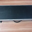 Černý transportní kufr s hliníkovými hranami a úchytem. V levém dolním rohu je kulaté stříbrné logo s nápisem "Custom Flight Cases". Povrch kufrů vyk…