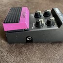 Kytarový efekt pedál v šedém kovovém provedení s růžovým ovládacím pedálem. Na zařízení jsou nápisy YAMAHA FL-10M, FLANGER a popisky ovládacích prvků…