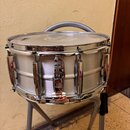 Stříbrný snare drum s kovovým korpusem a chromovaným obručováním. Na horním obruči je nápis Pearl SuperHoop LX. Nástroj vykazuje známky používání v p…