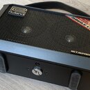 Černý přenosný stereo zesilovač s kovovou mřížkou reproduktorů a úchytem. Na horní části je logo Roland a červeno-zlatý štítek s nápisy MOBILE CUBE,…