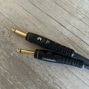 Dva černé kable s pozlacenými 6,3mm jack konektory. Na obou konektorech je bílý nápis D'Addario a u horního kabelu je navíc nápis SHIELDED END. Povrc…