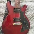 Elektrická kytara s červeným lakovaným korpusem a černým pickguardem. Nástroj má dva humbuckery, jeden tónový potenciometr a jeden přepínač. Na přilo…