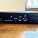 Zadní strana černého audio rozhraní s nápisem Focusrite®. Zařízení obsahuje napájecí vypínač, USB port, optický vstup s nápisem OPTICAL IN, dva MIDI…