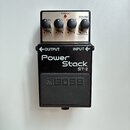 Kytarový efekt pedál značky BOSS, model Power Stack ST-2. Zařízení má černý kovový korpus s nápisy OUTPUT a INPUT u konektorů. Horní část tvoří stříb…