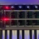 Detailní pohled na ovládací panel syntetizátoru micro KORG SYNTHESIZER/VOCODER. Panel je stříbrný s množstvím černých potenciometrů, tlačítek a nápis…