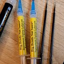 Na fotografii jsou čtyři předměty položené na dřevěném povrchu. Vlevo je bílý gel v černém plastovém aplikátoru s nápisy SUPERLUBE GEL PEN a logem D.…