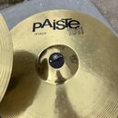 Zlatý kovový činel s koncentrickými drážkami. Na povrchu je černý nápis pAiste 101 BRASS a text 16" CRASH. Povrch je lesklý, v centru je vidět černá…