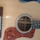 Detailní pohled na korpus akustické kytary se světlou deskou a tmavým hmatníkem. Na těle je umístěn výrazný hnedý pickguard s mramorovaným vzorem. Ko…