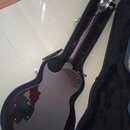 Tmavě červená elektrická kytara v černém tvrdém kufru. Na hlavě hmatníku je vidět nápis "Gibson". Povrch nástroje je vysoce lesklý a bez viditelných…