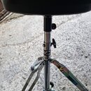 Černý polstrovaný sedák na chromovaném třínohém stojanu. Na kovovém kmenu je viditelné logo s nápisem Mapex. Povrch sedáku i chromované části jsou v…