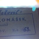 Detailní záběr na papírový štítek s textem. Na štítku je napsáno: „- Zhotovil - JOSEF TOMÁŠEK, houslař v RYDŽOV. Rok 1953.“. Text je umístěn v jednod…