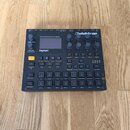 Šedý digitální sampler a sekvencer značky Elektron, model Digitakt. Zařízení má černé ovládací prvky, včetně 16 podsvícených padů a několika otočných…