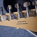Detail hlavy elektrické kytary z anýžového dřeva s šesti chromovanými ladicími mechanismy. Na zadní straně hlavy je černý nápis ISJ2213676 a pod ním…