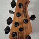 Záběr na hlavu pětstrunné basové kytary z přírodního dřeva s černými ladičkami. Na dřevě je černý nápis MUSIC MAN StingRay 5 a nad ním menší text ERN…