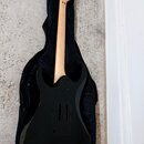 Černá elektrická kytara s jasným dřevěným hmatníkem a hlavou, položená v černém softcasu. Na hlavě nástroje je viditelný nápis "Squier". Povrch kytar…