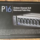 Fotografie zachycuje černou krabici s produktem P16 Sixteen Channel XLR Balanced Patch Bay. Na obalu je zobrazen obraz přístroje s řadou konektorů a…