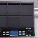 Černý elektronický bicí pad s devíti čtvercovými polštáři v mřížce 3x3. Na spodním panelu jsou nápisy Millenium a NonaPad, malý displej, několik tlač…