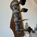 Zadní strana hlavy basové kytary z přírodního dřeva s chromovanými ladicími kolíky. Na každém z kolíků je vyryto logo Fender. V horní části je nápis…
