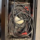 Černý plastový přepravní kufr, ve kterém jsou sbalené několik metrů černých kabelů s červenými konektory. Na spodní části kufrů je bílý štítek s nápi…