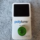 Bílý efekt pedál s černým displejem a zeleným plastovým ovratovcem. Na přední straně je modrý nápis polytune3 a pod ním text TRUE BUFFER. V dolní čás…