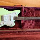 Světle zelená elektrická kytara v hnědém tvrdém kufru s purpurovým polstrováním. Kytara má bílý perleťový pickguard a na hlavě je nápis WOLF DupliTon…