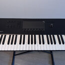 Černý MIDI kontrolér s klávesnicí umístěný na černém stojanu. Na horním panelu je nápis KONTROL S49 MK3, displej a řada ovládacích tlačítek a otočnýc…