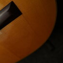 Detailní záběr na horní desku akustického nástroje z dřeva s viditnou sletovanou strukturou v hnědo-oranžovém odstínu. V levé části je vidět tmavý, p…