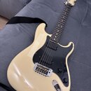 Elektrická kytara s krémovým povrchem, černým pickguardem a hnedým hmatníkem. Na hlavě je viditelné logo Fender. Nástroj má jednu humbuckerovou sníma…