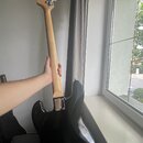 Fotografie zachycuje zadní stranu elektrické basové kytary s černým bodies a světlým dřevěným hmatníkem a hlavou. Na hlavě jsou čtyři stříbrné ladičk…
