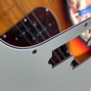 Detailní záběr na bílý plastový pickguard s vyřezanými otvory pro snímače a ovládací prvky. Pod pickguardem je vidět dřevěné tělo elektrické kytary v…