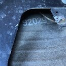 Detailní záběr na černý plastový nebo lakovaný povrch s odhraničeným výřezem. Uvnitř výřezu je na šedém, texturovaném povrchu viditelné bílé sériové…