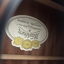 Detail vnitřní strany akustické kytary s oválnou papírovou štítkem. Na štítku je nápis Washburn, Since 1883 a označení Model No. WMJ75CEBM Serial No.…
