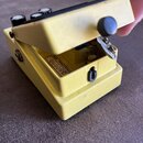 Žlutý kytarový efekt pedál v otevřeném stavu. Uvnitř je vidět bílá nálepka s černým číslem 380600 a nápisem products of Boss Japan. Povrch pedálu vyk…
