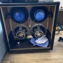 Otevřený černý reproduktorový box s dřevěným vnitřkem, ve kterém jsou osazeny čtyři reproduktory. Horní dva mají modré kryty s bílým nápisem EMINENCE…