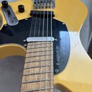 Detail elektrické kytary v žluté barvě s černým pickguardem a hnedou hmatníkem. Na pickguardu je bílý nápis "Gothar strandberg*". Nástroj má stříbrný…