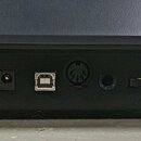 Detail zadní strany černého elektronického zařízení s řadou konektorů. Jsou zde vidět porty s nápisy DC 9V (center +), USB-to-Host, MIDI OUT, SUSTAIN…