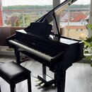 Černé digitální piano v provedení křídla s přiloženou černou polstrovanou stolečkou. Na rightové straně klávesnice je viditelný nápis KORG. Nástroj m…