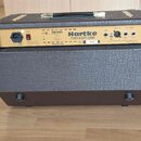 Zadní strana akustického komba v hnědém texturovaném potahu s kovovými rohy. Na zlatém ovládacím panelu je nápis Hartke 75 WATT ACOUSTIC Ribbon a web…