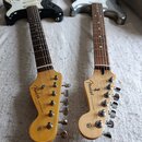 Dvě elektrické kytary typu Stratocaster položené vedle sebe na světlém textilu. Levá kytara má černé tělo s bílým pickguardem a pravá kytara má stříb…